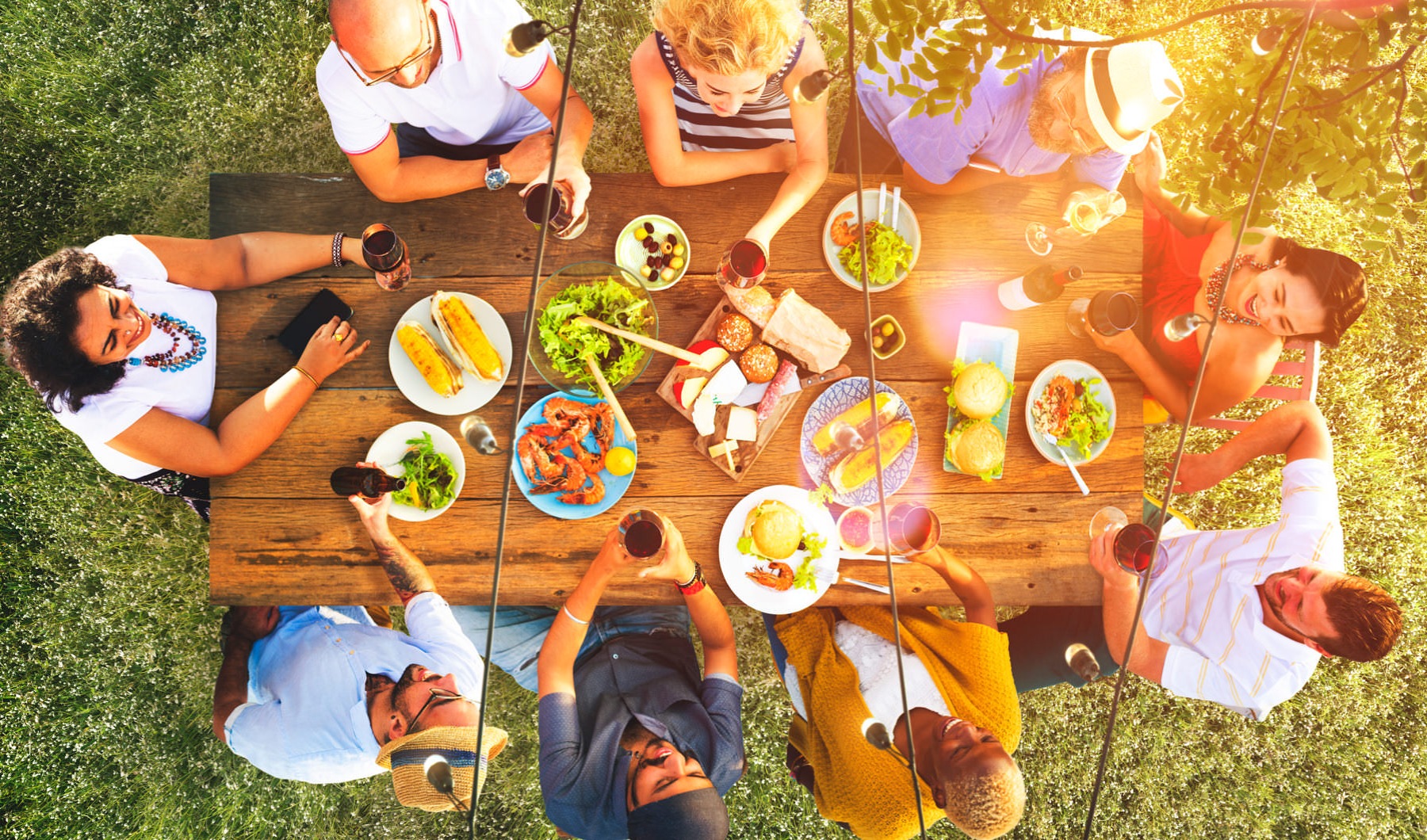 family and friends sitting and laughing outdoors around a large table of food 